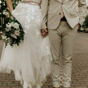 man in gray suit jacket and woman in white wedding dress holding bouquet of white flowers